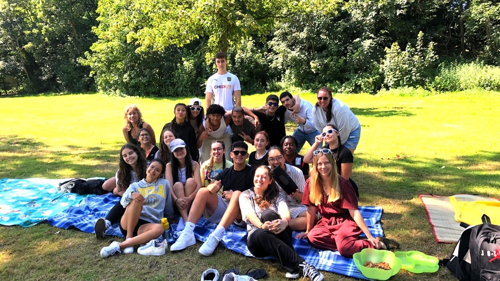 Gruppe junger Menschen aus verschiedenen Ländern sitzt auf Picknickdecke im Park., Link auf Internationale Jugendarbeit – Angebote für junge Menschennge u