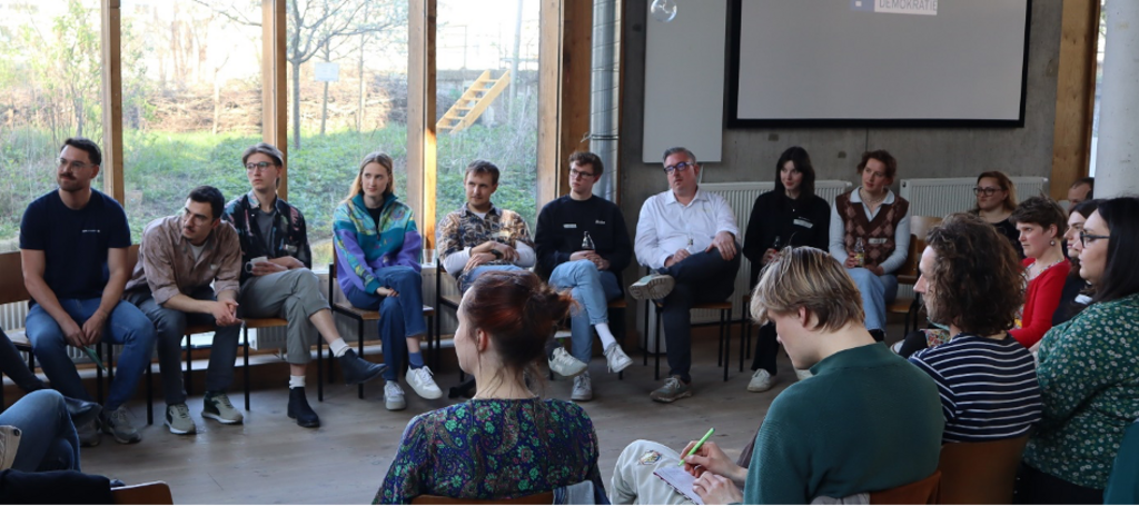 Gesprächsrunde. Mehrere Personen sitzen auf Stühlen im Kreis. 