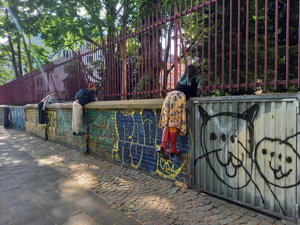 Drei Menschen die über eine Graffiti besprühte Mauer lehnen. 