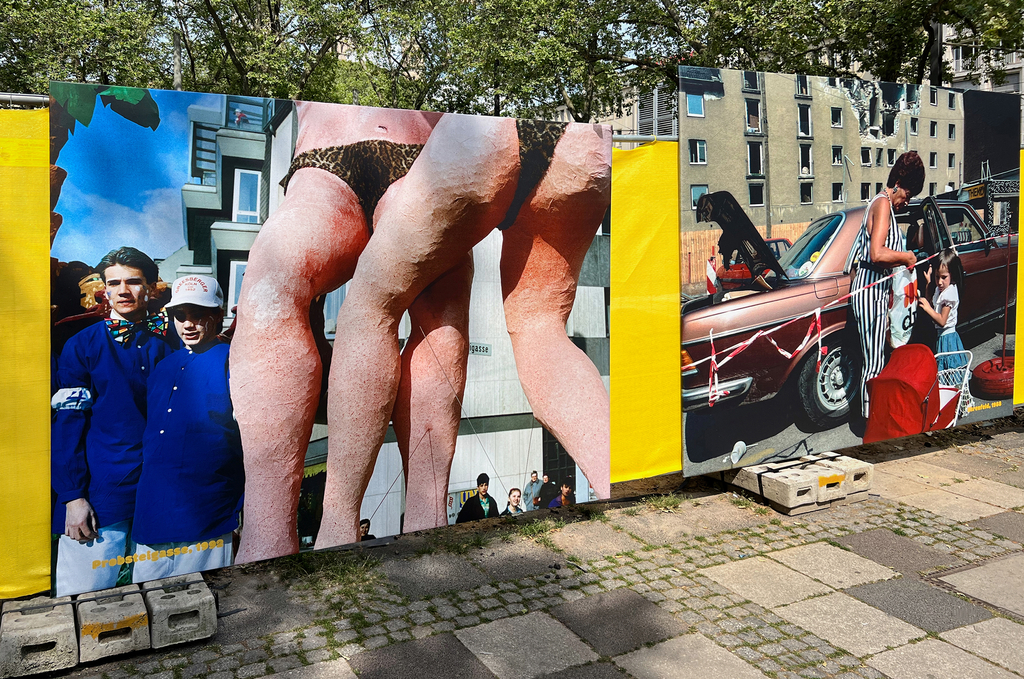 Foto mit zwei großen Ausstellungsplakaten von Wolfgang Zurborn . Linkes Plakat: Beine von zwei große Figuren in Unterwäsche im Vordergrund. Im Hintergrund stehen zwei Jugendliche. Rechtes Plakat: Eine Frau steht mit einem Kind vor einem Auto hinter einer Absperrung. 