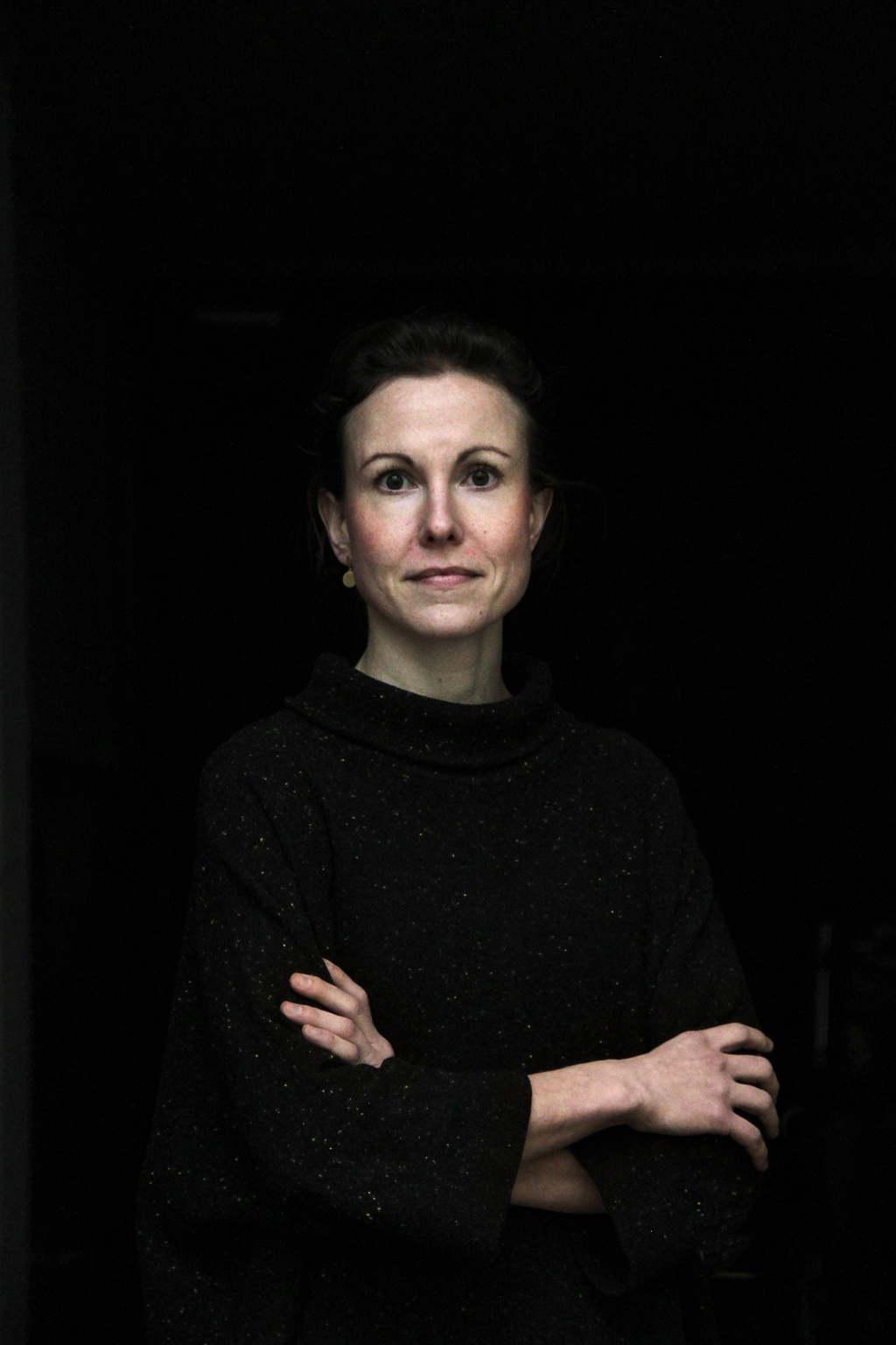 Bild einer Frau in Schwarz gekleidet vor schwarzem Hintergrund.