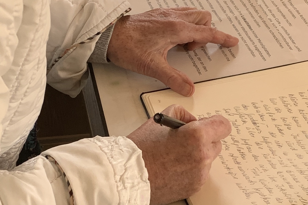 Foto von einem Buch, in welches eine Person einen handschriftlichen Eintrag macht