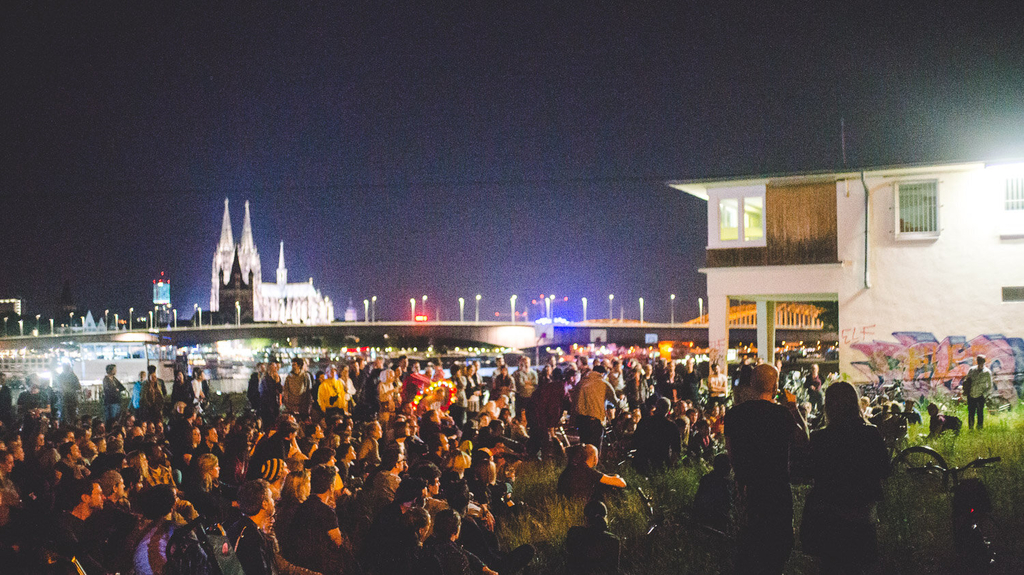 Foto von einer Menschenmenge, die einen Film schaut. Im Hintergrund ist der Dom zu erkennen.
