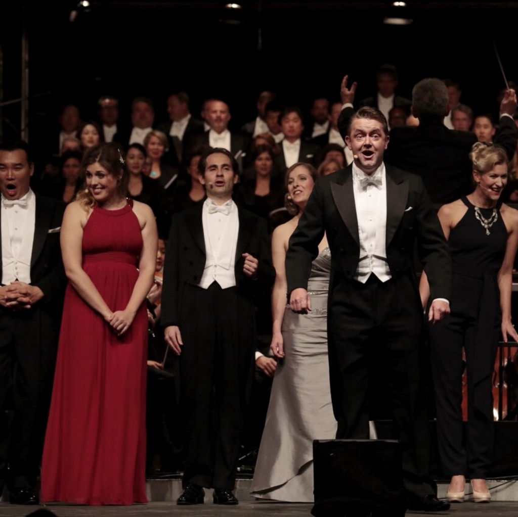 Sängerinnen und Sänger in festlicher Kleidung auf der Bühne der Oper Köln