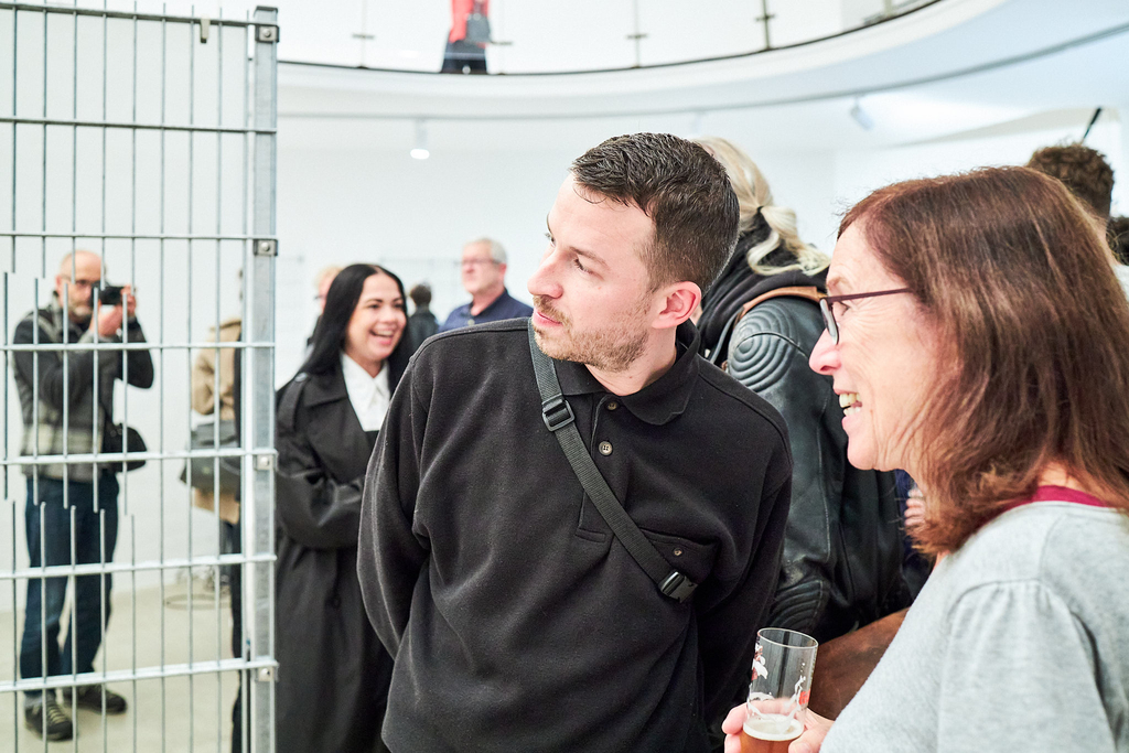 Preisträger Mathias Weinfurter und ein*e Besucher*in im Gespräch. Im Hintergrund sind mehrere Gäste zu sehen