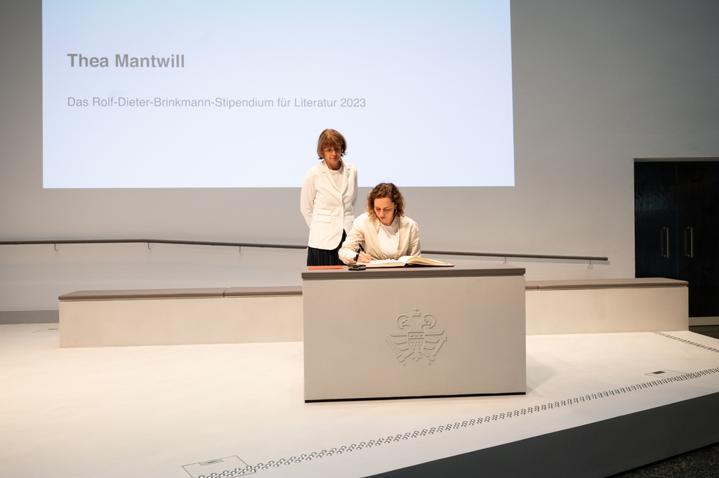 Thea Mantwill trägt sich ins Gästebuch ein. Neben ihr steht Henriette Reker.