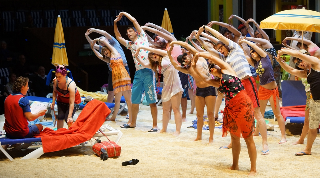 Auf der Bühne ist eine Strandszene aufgebaut, Badegäste machen Gymnastik-Übungen