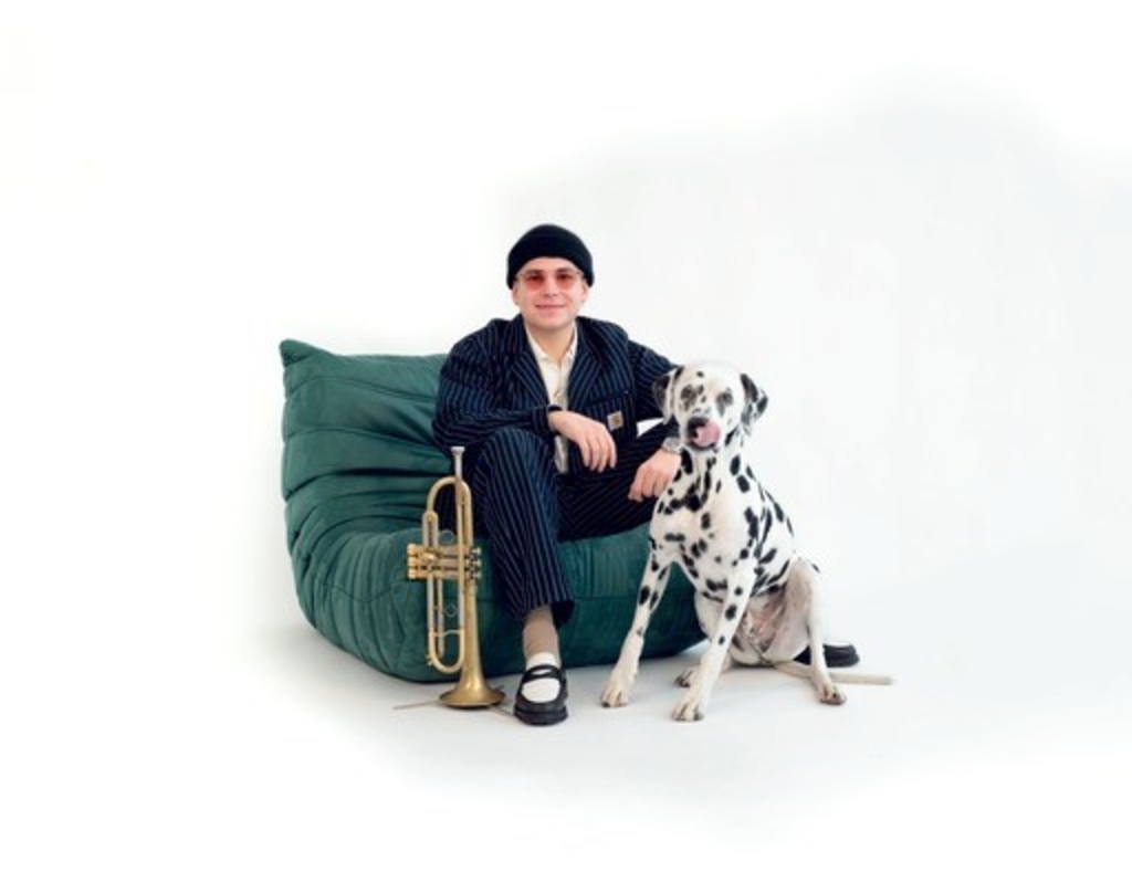 Ein Musiker sittzt auf einem Sitzkissen, neben Ihm seinen Trompete und ein Hund