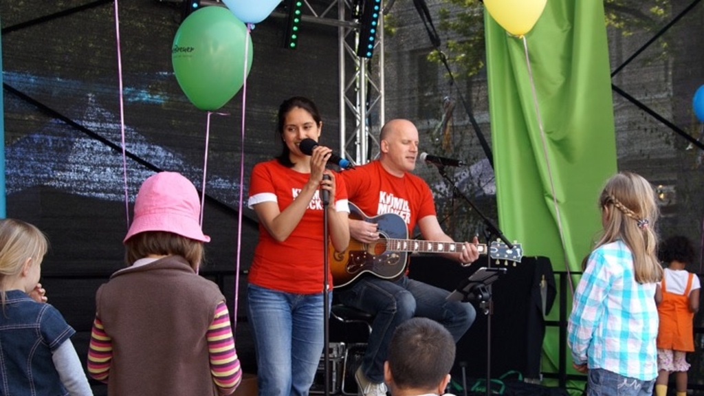Frau mit Mikrofon und Mann mit Gitarre auf einer Bühne