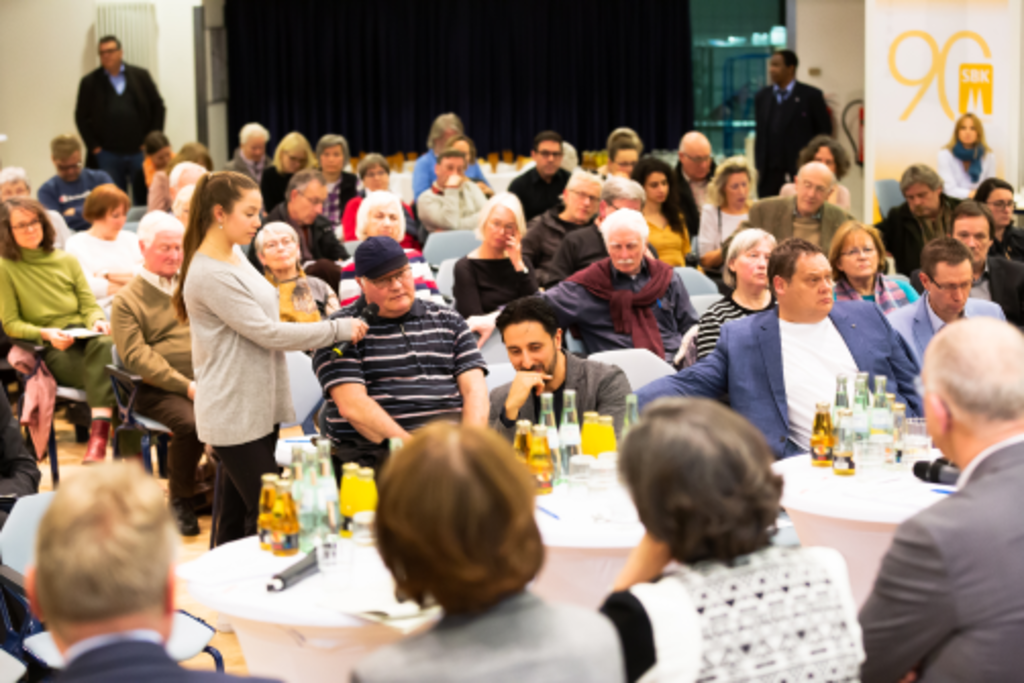 Ein Mann aus dem Publikum wird von der Moderatorin beim Stadtgespräch in Nippes interviewt.