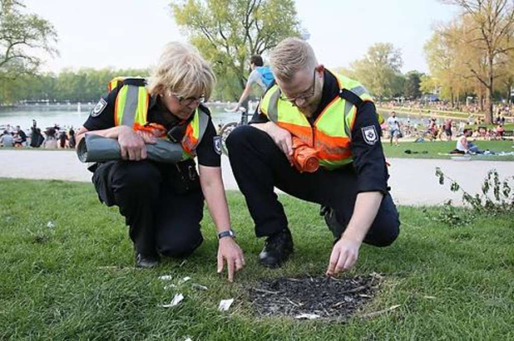 Zwei Beamte vom Ordnungsdienst begutachten eine verbrannte Grasstelle