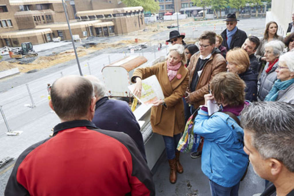 Eine Gruppe von Menschen steht vor der Baustelle. Eine Mitarbeiter erläutert anhand von einer Skizze die Planung.
