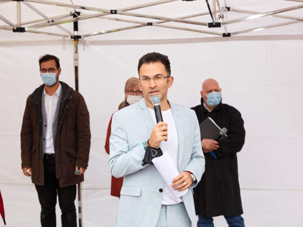 Moderator Fatih Cevikkollu mit Mitgliedern des Chorweiler Runden Tischs Frieden im Hintergrund