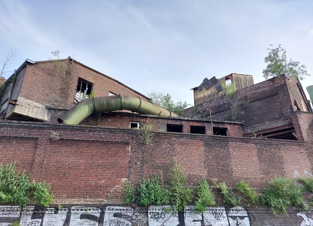 Werksmauer am Auenweg mit dahinterliegenden Industriegebäuden