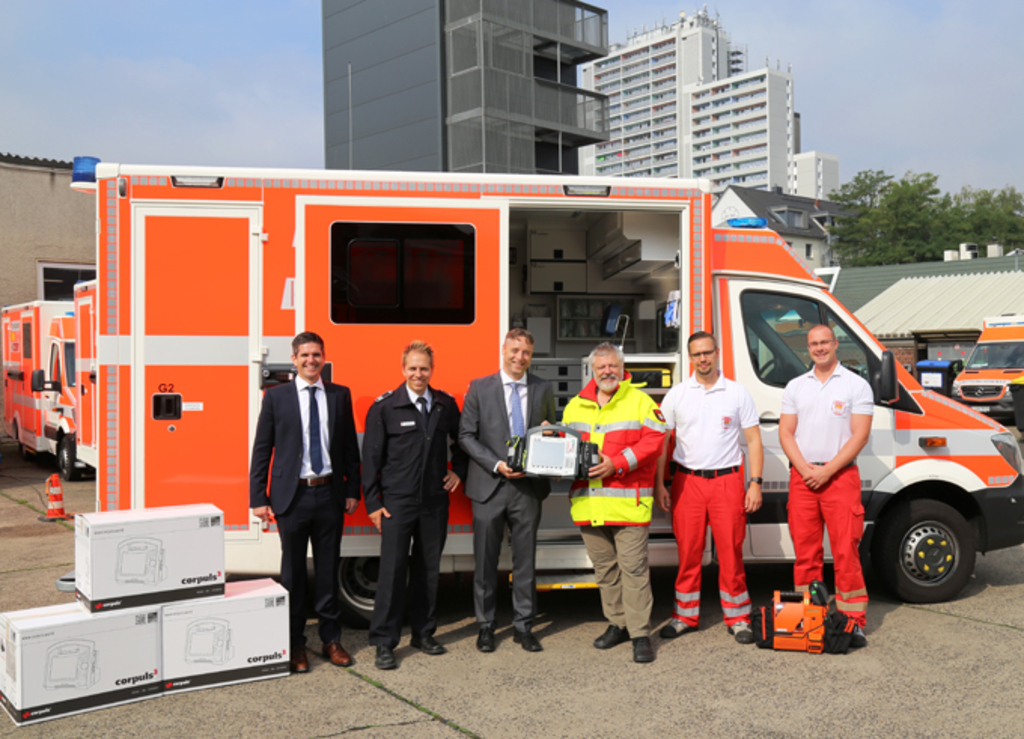Gruppenfoto vor einem Rettungswagen mit dem neuen Gerät zum Patientenmonitoring