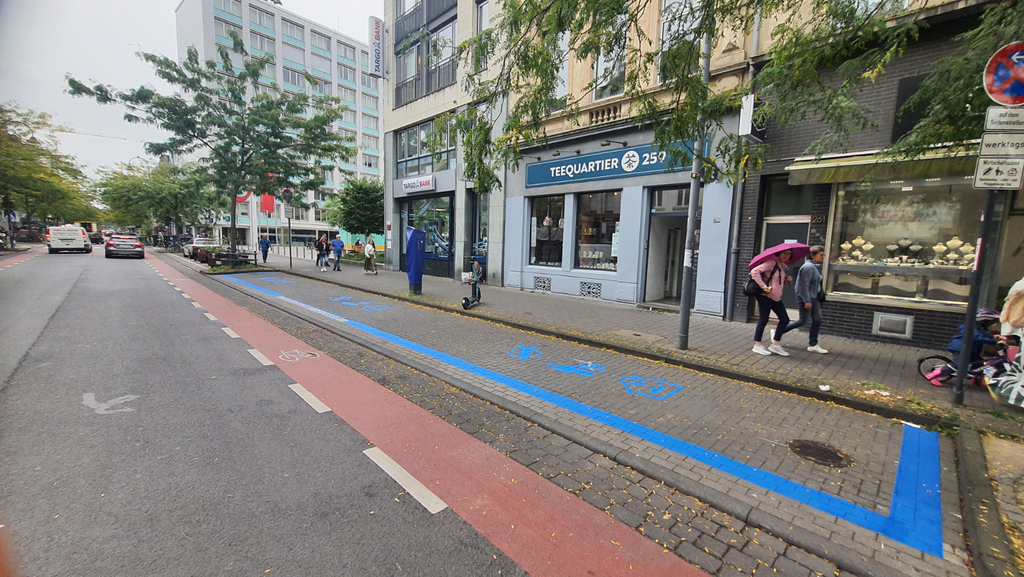 Foto der Venloer Straße, die Parkplatzbucht ist als Wirtschaftszone blau ausgezeichnet.