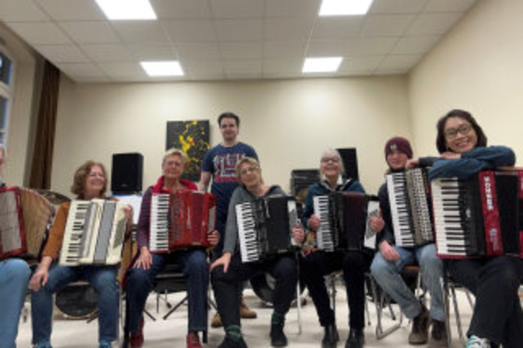 7 Akkordeonistinnen mit ihren Akkordeons in ihrem Probenraum, im Hintergrund der Leiter Vadim Baev, Link auf Akkordeon-Ensemble "Diskant risskant" - Stadt Köln