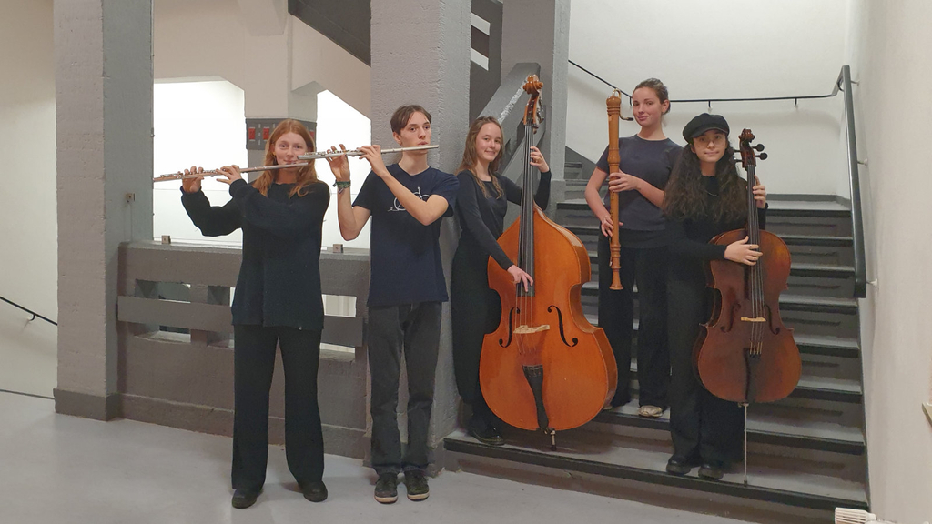 Fünf junge Musiker*innen mit zwei Querflöten, einer Bassblockflöte, einem Cello und einem Kontrabass in einem Treppenhaus
