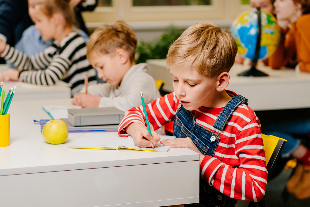 Gruppe von Kindern sitzen in einem Klassenzimmer und schreiben in ein Heft., Link auf Karten zu Bildung und Schulen