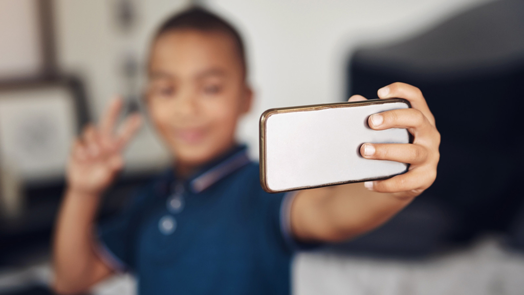 Junge hält Mobiltelefon in der Hand umd macht ein Selfie.