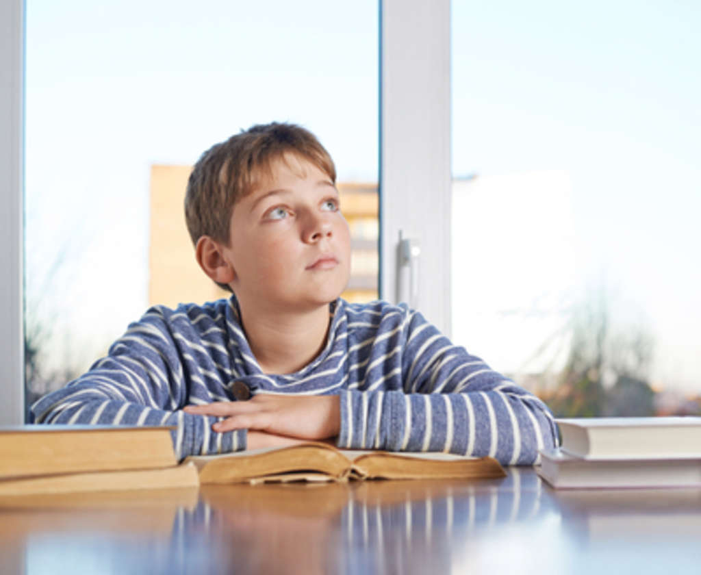 Junge sitzt über Bücher und träumt vor sich hin