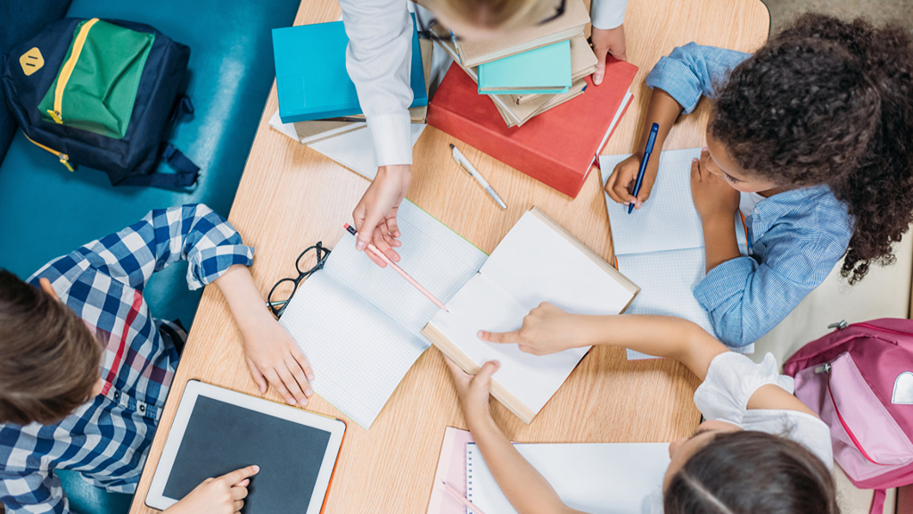 Blick von oben auf Lehrekraft und jungen Schüler*innen, die gemeinsam Hausaufgaben machen