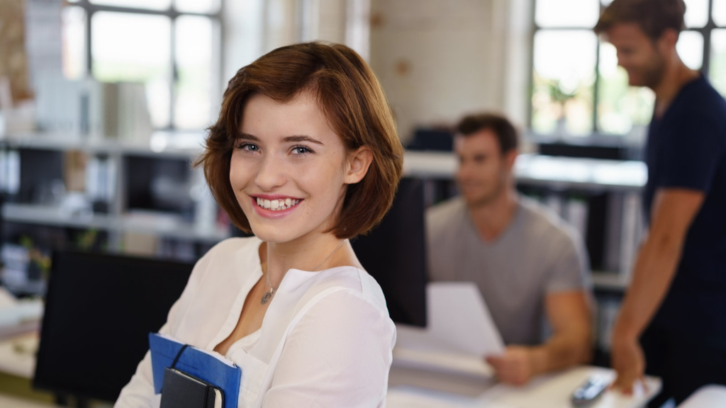 In die Kamera lächelnde, junge Mitarbeiterin im Büro