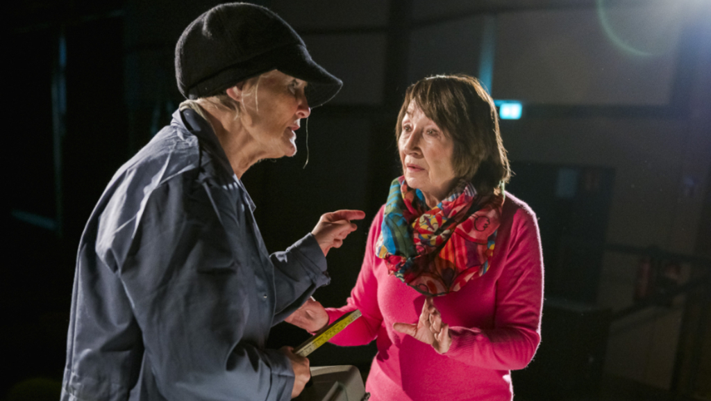 Links eine Person mit einer Mütze und Mantel, rechts eine ältere Dame mit fragendem Gesichtsausdruck