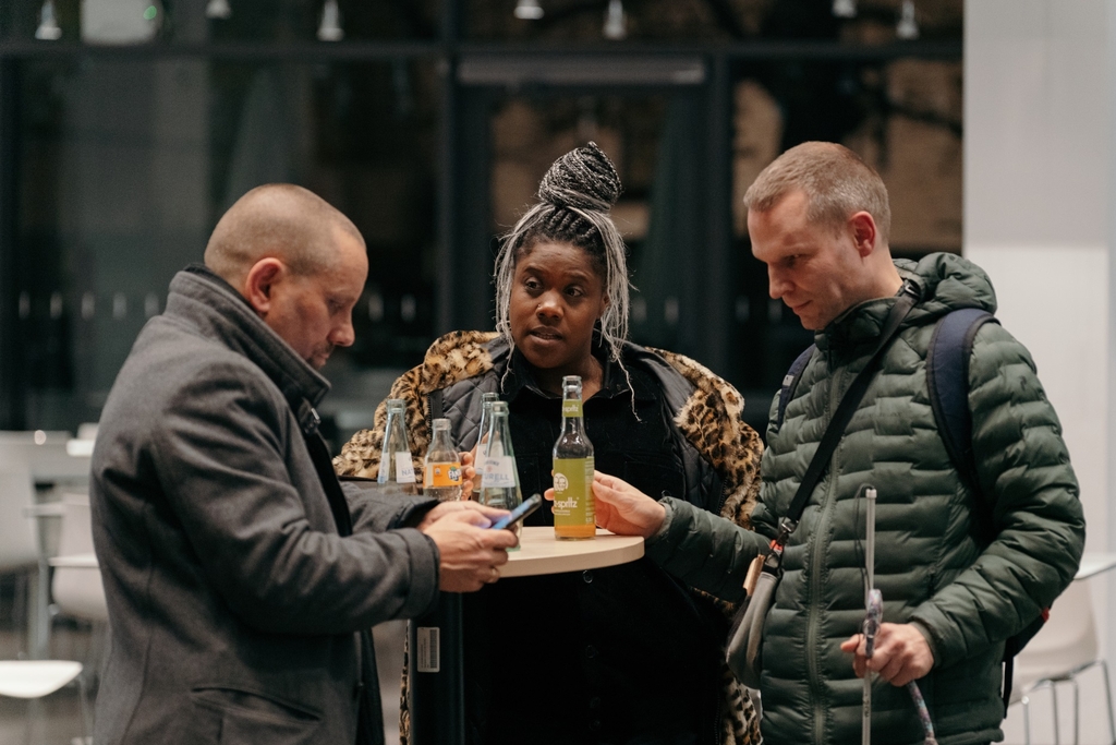 Drei Personen stehen um einen Stehtisch.