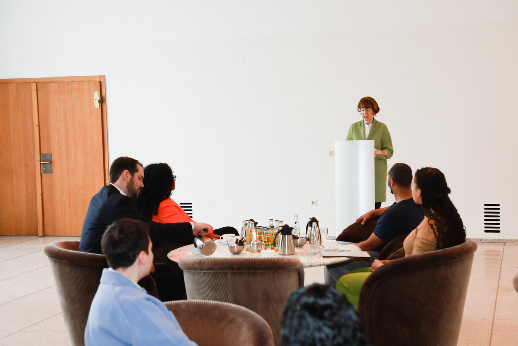 Die Oberbürgermeisterin Henriette Reker steht an einem Pult und spricht. Vor ihr sitzen Mitglieder aus dem Expert*innengremium und andere in Sesseln. Die Köpfe sind auf die Bühne gerichtet. 