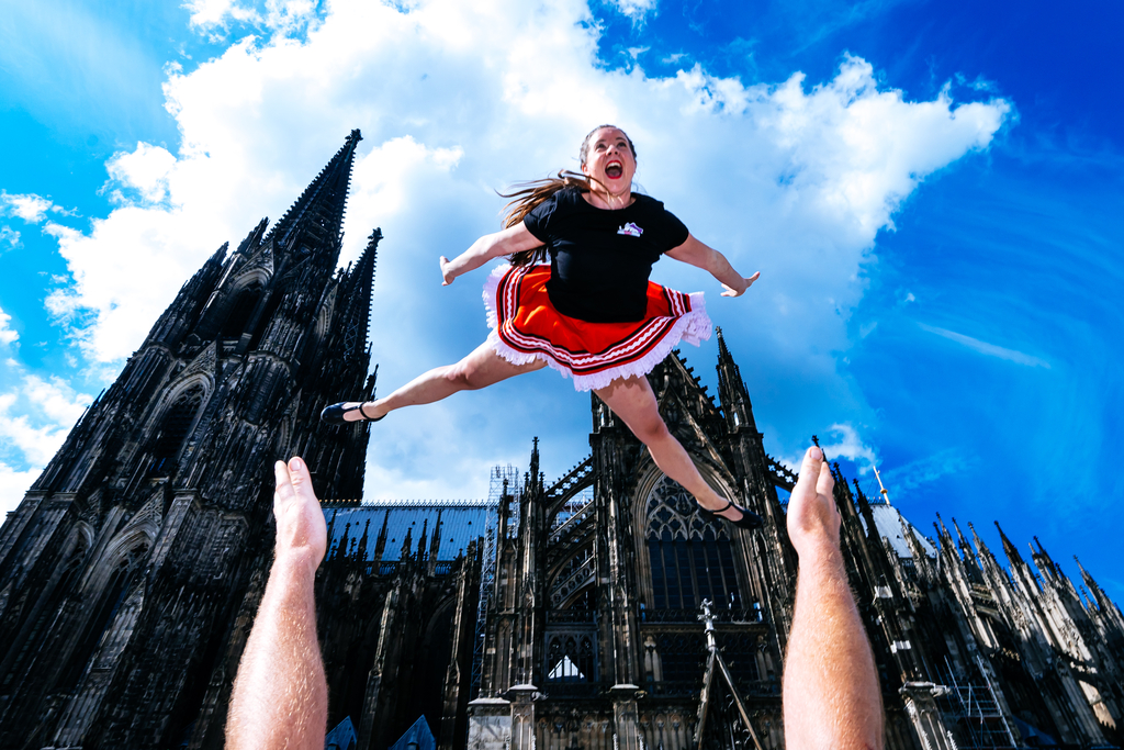 Ein Tanzgruppenmitglied wird in die Luft geworfen, im Hintergrund der Kölner Dom