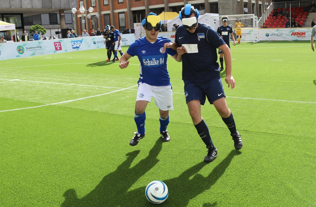 Zwei Blindenfußballer kämpfen auf dem Fußballfeld um den Ball