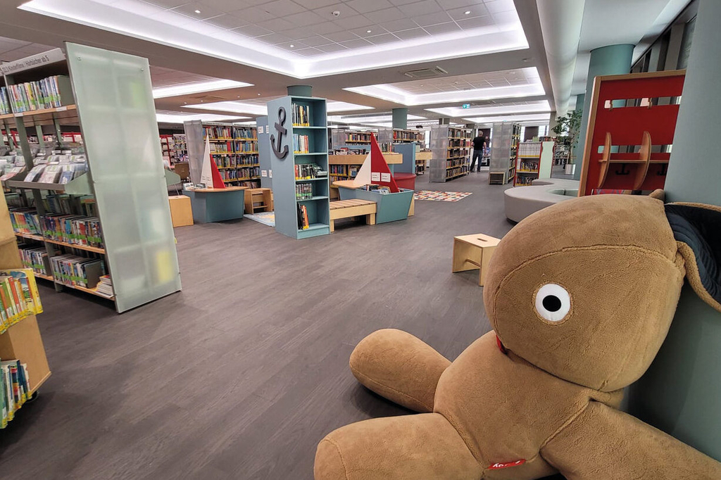 Im Vordergrund ein riesiger Plüschhase, im Hintergrund Bücherregale und ein Holzschiff, Link auf Kinderbibliothek - Stadt Köln