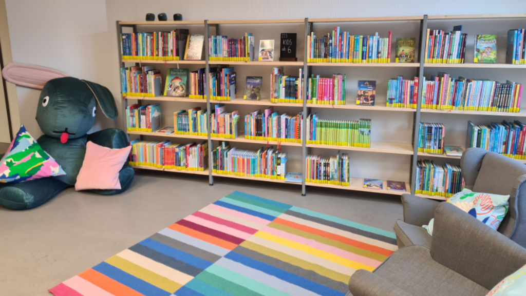 Foto der neugestalteten Stadtteilbibliothek Ehrenfeld mit neuem Bücherregal und einer Kuschelecke mit großem Plüschhasen, Teppich und Sesseln