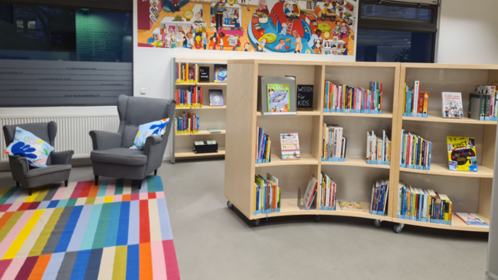 Foto der neugestalteten Stadtteilbibliothek Ehrenfeld mit neuen Bücherregalen, Teppich und zwei Sesseln