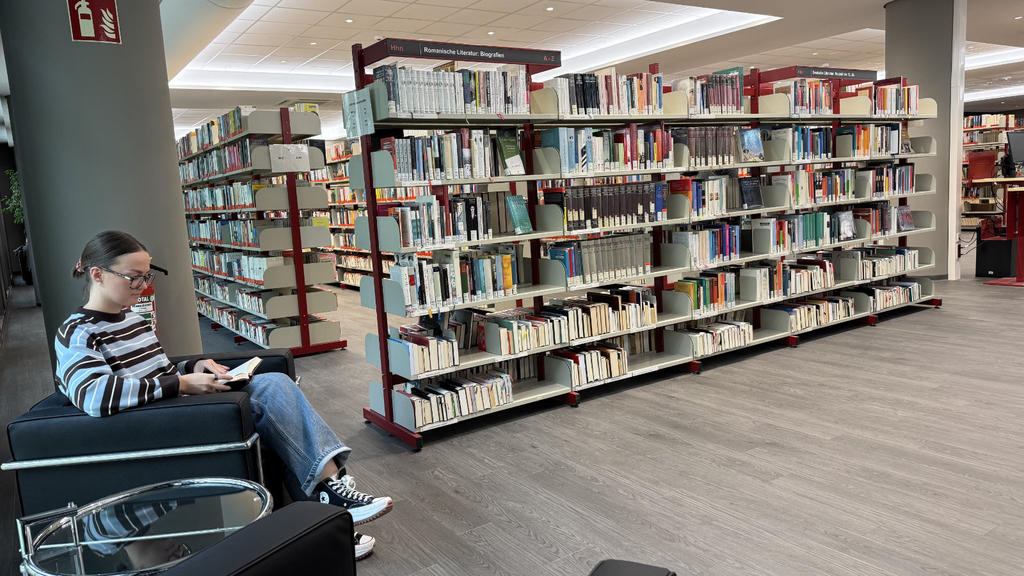 Frau sitzt lesend im Sessel neben Bücherregalen im Interim der Stadtbibliothek 