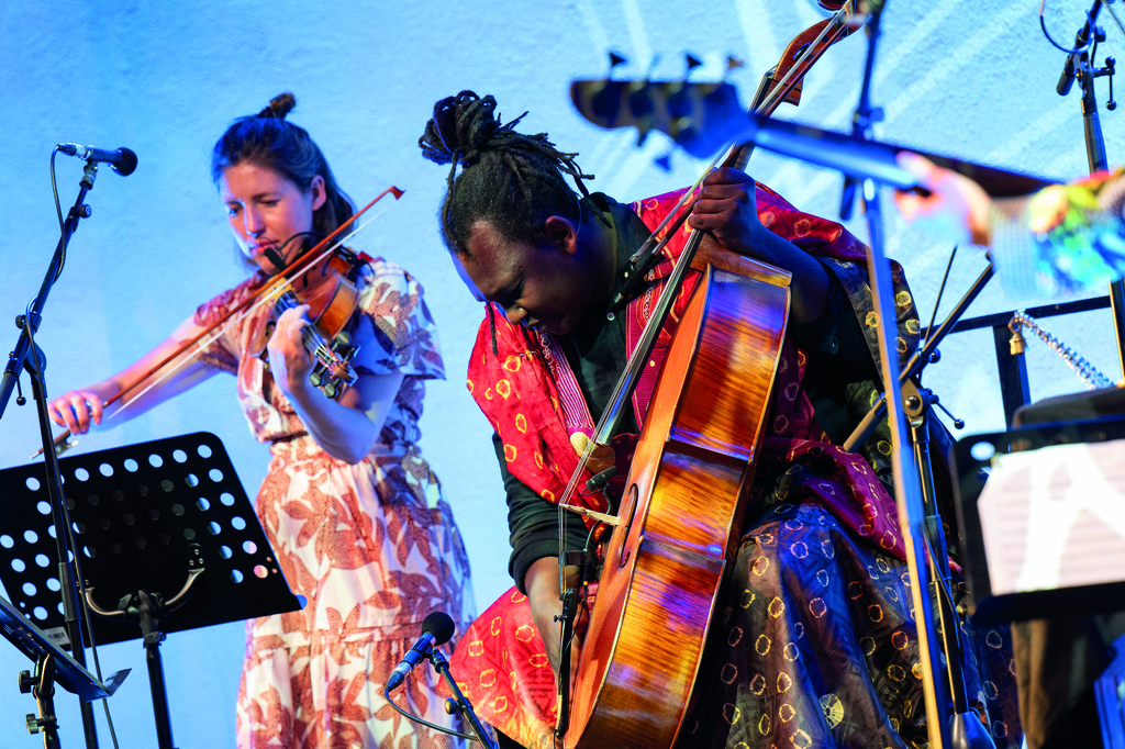 Im Vordergrund ist ein Mann abgebildert, der Kontrabass spielt, schräg dahinter steht eine Frau, die Geige spielt.