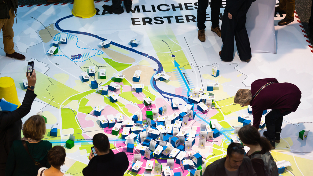 Das Foto zeigt eine Teilnehmende des zweiten Zukunftsforums an der großen Bodenkarte des Zielbildes der Kölner Stadtstrategie.