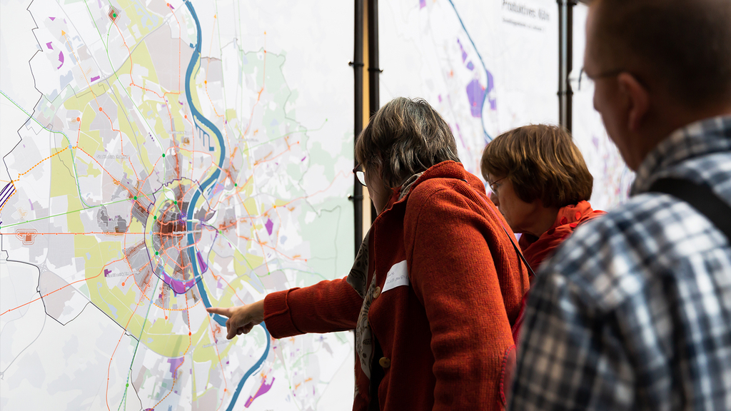 Das Foto zeigt eine teilnehmende Personenen des zweiten Zukunftsforums, die sich an einem Kartenaushang informieren.