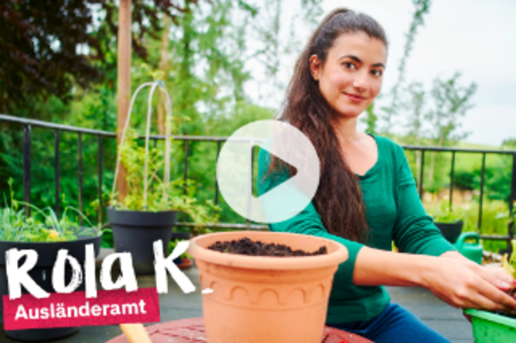 Foto von Rola, sie lächelt in die Kamera und pflanz eine Blume ein, mit Playbutton und Schriftzug "Rola K. Auslä#nderamt", Link auf Die Kölnmacher*innen: Rola - YouTube