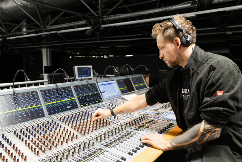 Ein Mann sitzt vor einem Mischpult und stellt etwas ein.