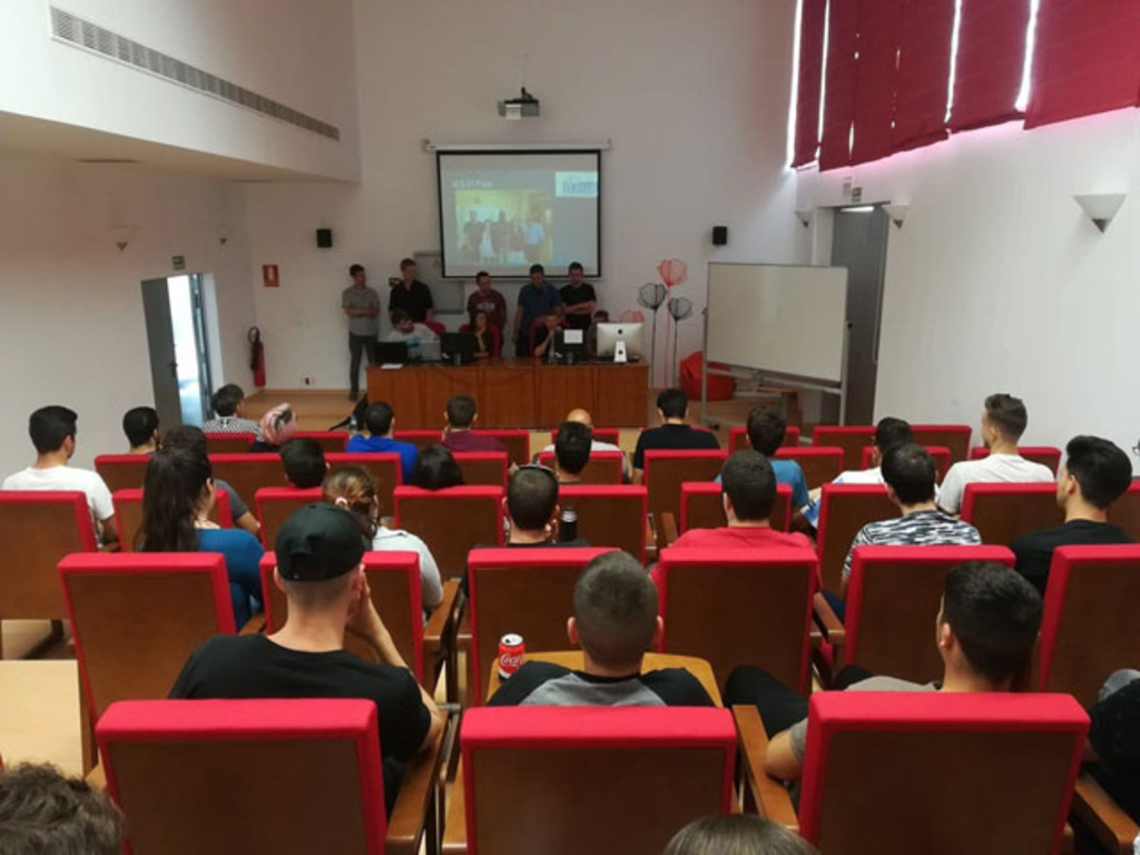 Azubis sitzen in einem Vortragsraum auf roten Sesseln vor einer Leinwand