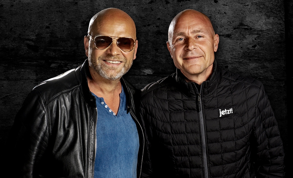 Zwei Männer mit Glatze vor dunklem Hintergrund