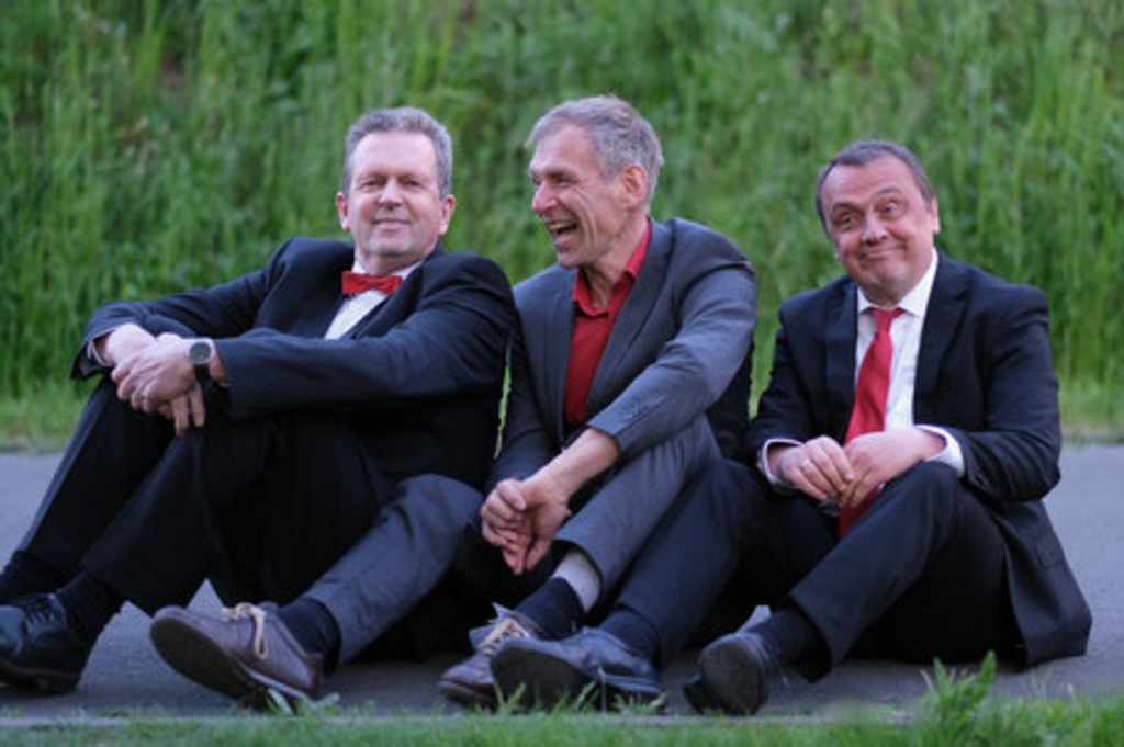 Die drei Kabarettisten sitzen lachend auf der Erde