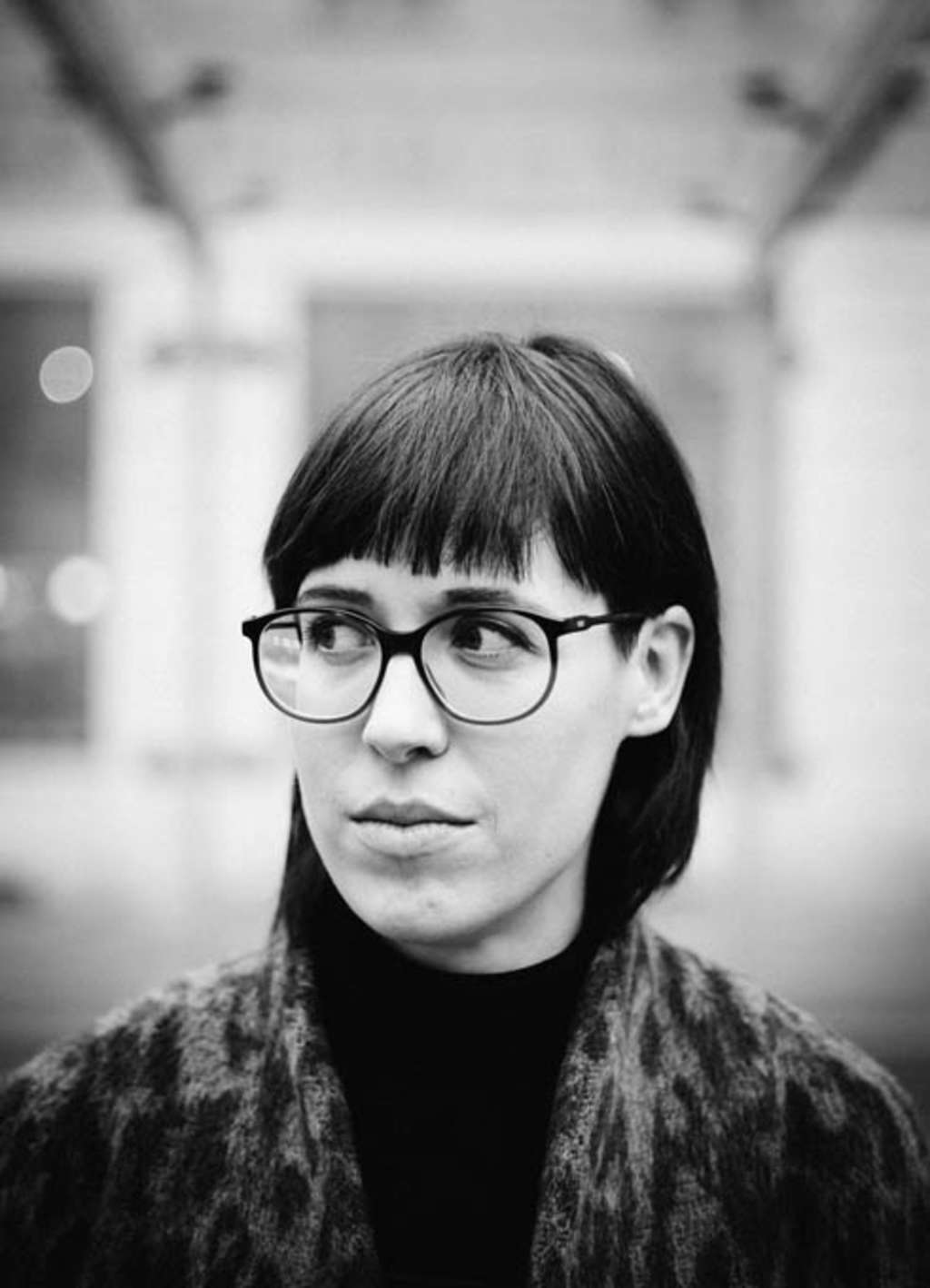 Frau mit großer runder Brille, Rollkragenpullover und flauschiger Jacke schaut zur Seite.