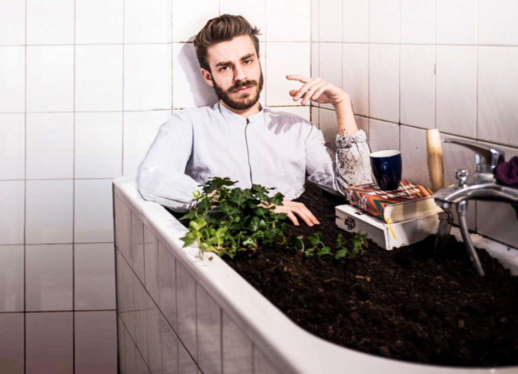 Kindler - Mann im weißen Hemd sitzt in einer Badewanne voller Erde