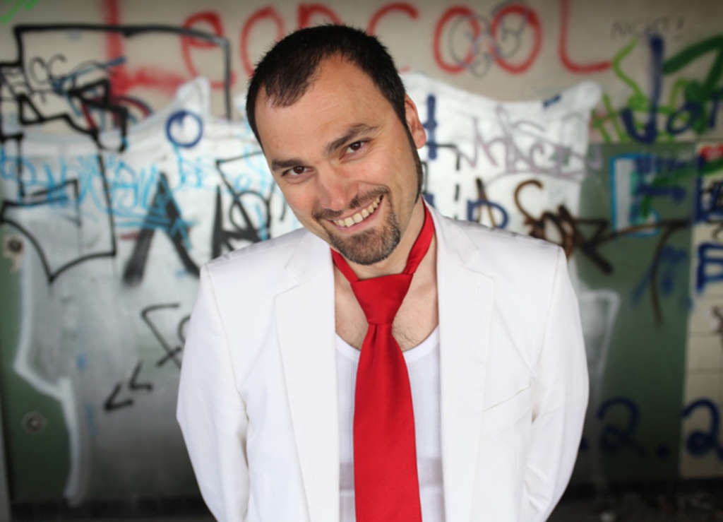 Danko Rabrenović mit weißem Jacket und roter Krawatte. Lächelt in die Kamera.