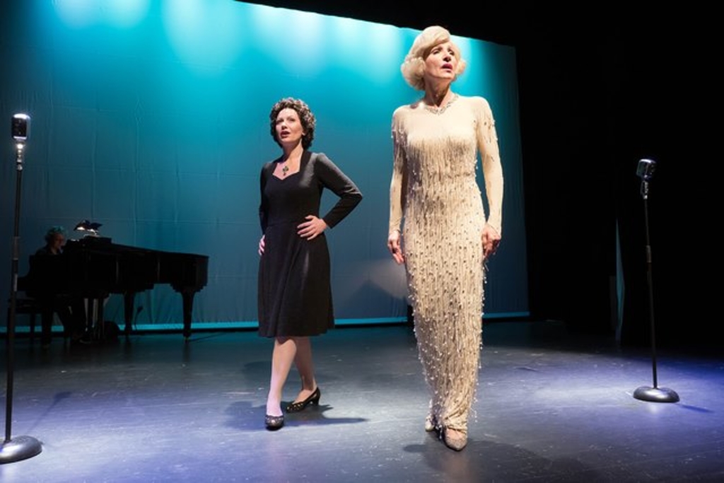 Zwei Frauen auf der Bühne, eine dunkelhaarig in blauem Kleid, die Andere blond in weißem Kleid