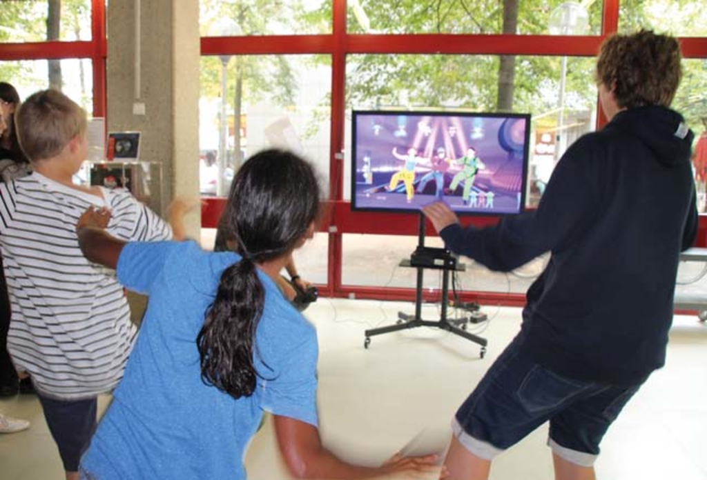 3 Kinder von hinten fotografiert beim Tanzen mit Just Dance auf einer Spielkonsole