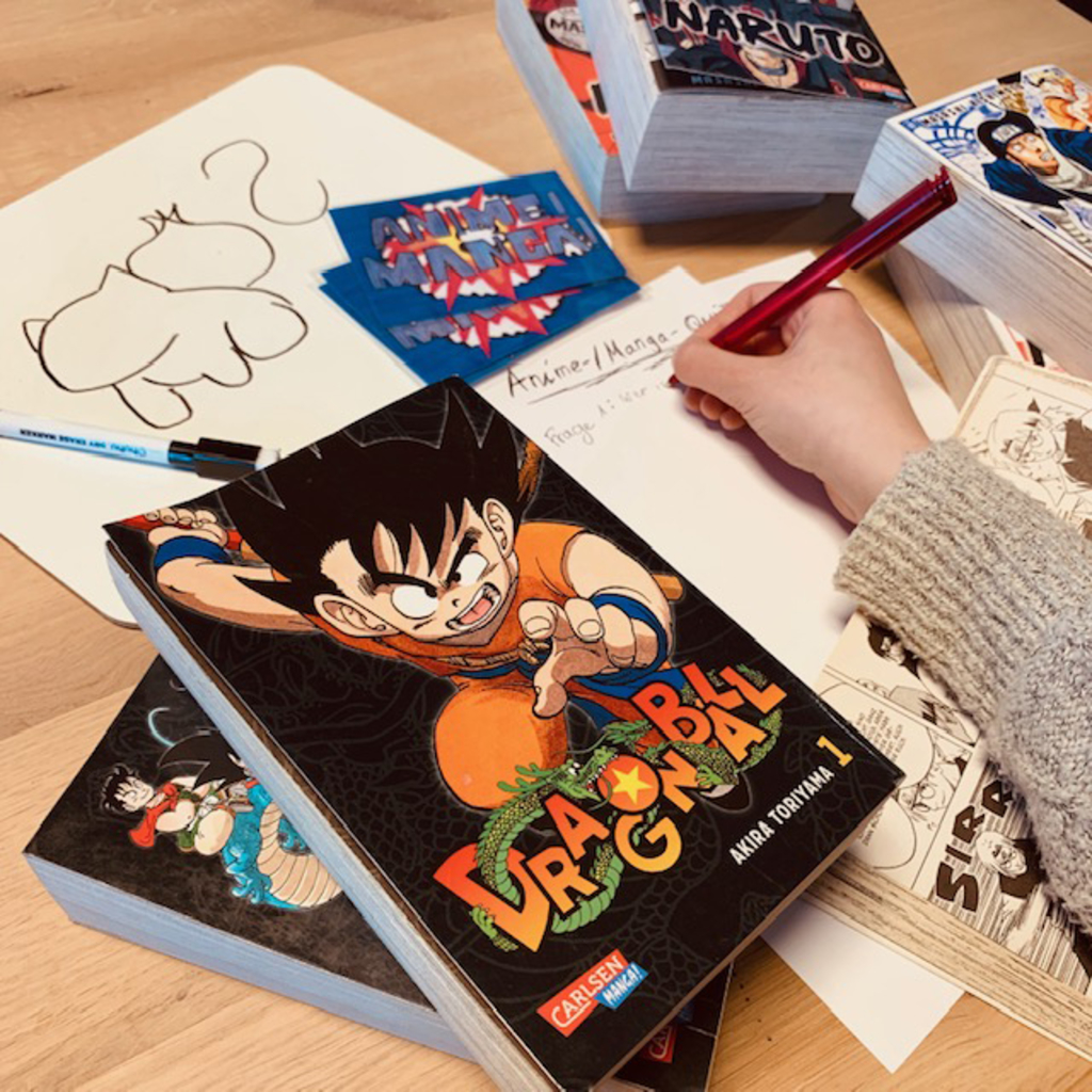 Manga Quiz - Manga Bücher, dazwischen eine Hand mit Stift, die schreibt